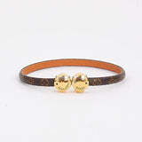 A Louis Vuitton bangle bracelet featuring a brown monogram canvas band with a tan leather interior and two gold-tone heart charms engraved with the brand name.