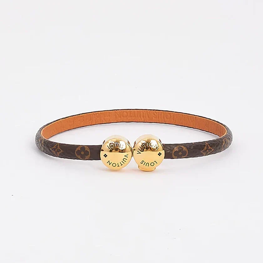 A Louis Vuitton bangle bracelet featuring a brown monogram canvas band with a tan leather interior and two gold-tone heart charms engraved with the brand name.