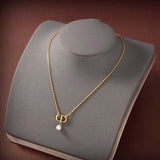 Gold necklace with a pearl pendant on a gray jewelry display.