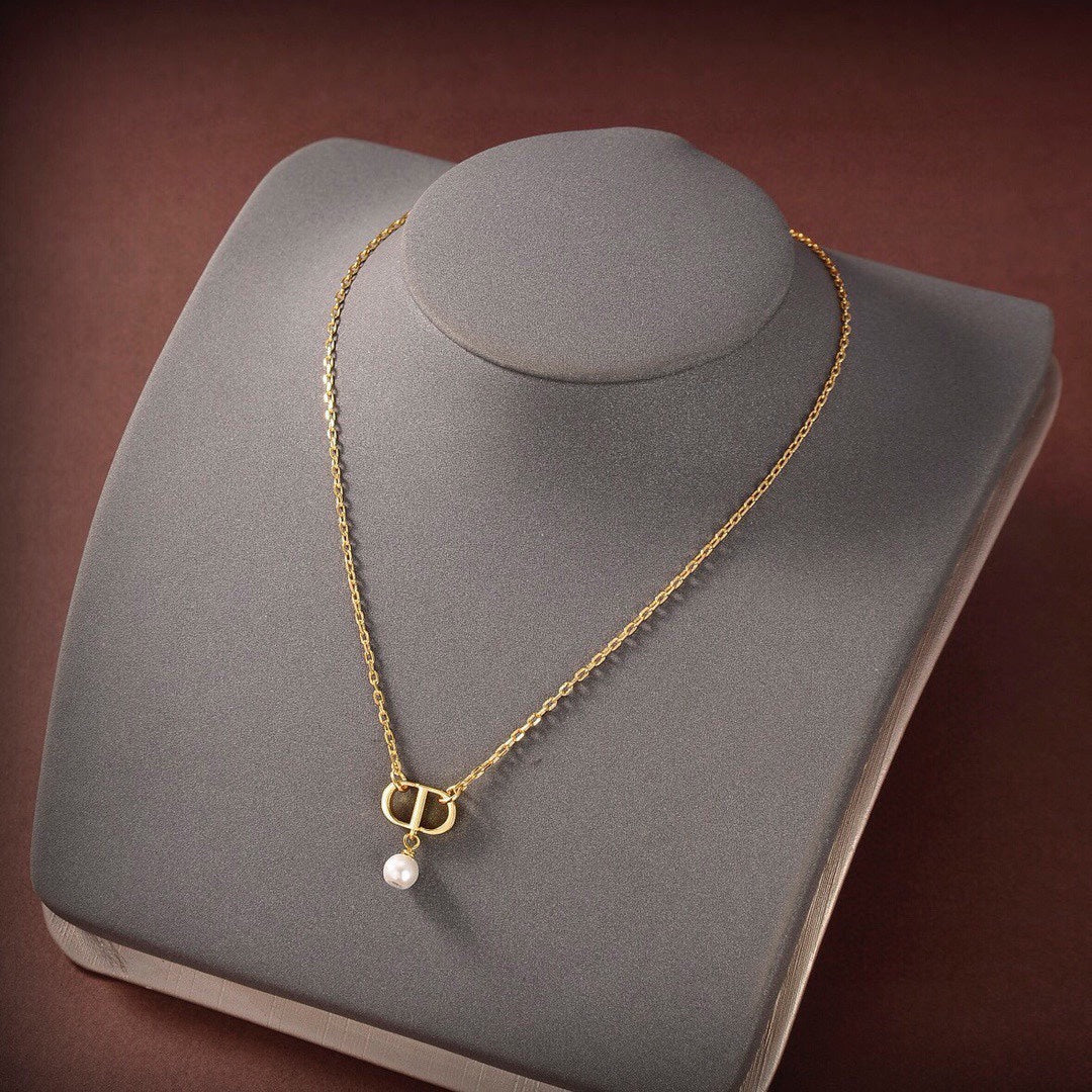 Gold necklace with a pearl pendant on a gray jewelry display.