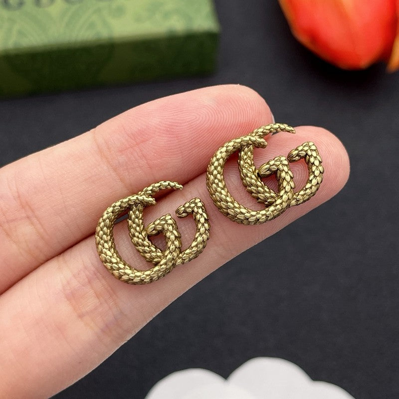 Gold earrings held between fingers with a dark background