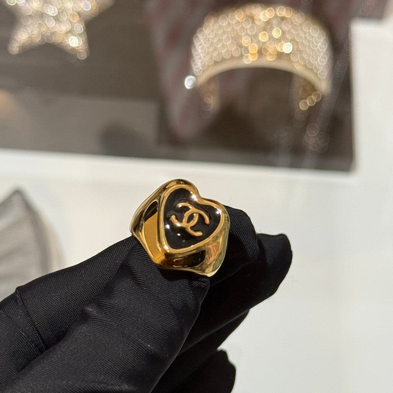 Gold heart-shaped ring with Chanel logo held by a gloved hand against a blurred background.
