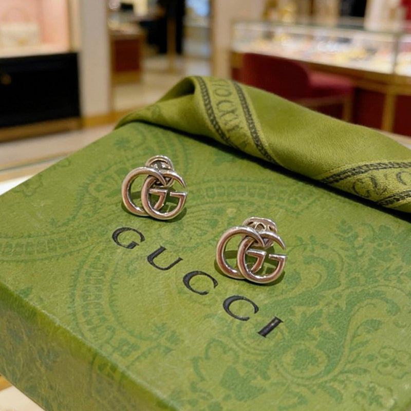 Silver Gucci earrings on a green Gucci box in a store setting