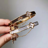 Two gold bracelets with floral and lock designs on a neutral background