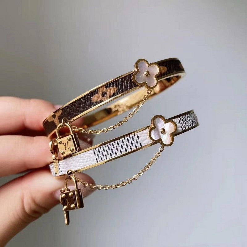 Two gold bracelets with floral and lock designs on a neutral background