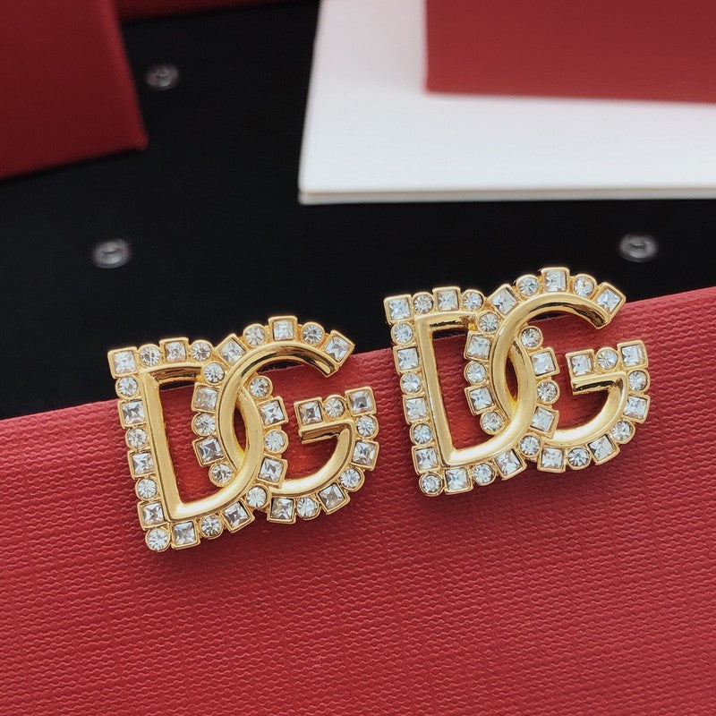 Gold DG earrings with rhinestones on a red surface