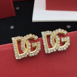 Gold DG earrings with rhinestones on a red surface