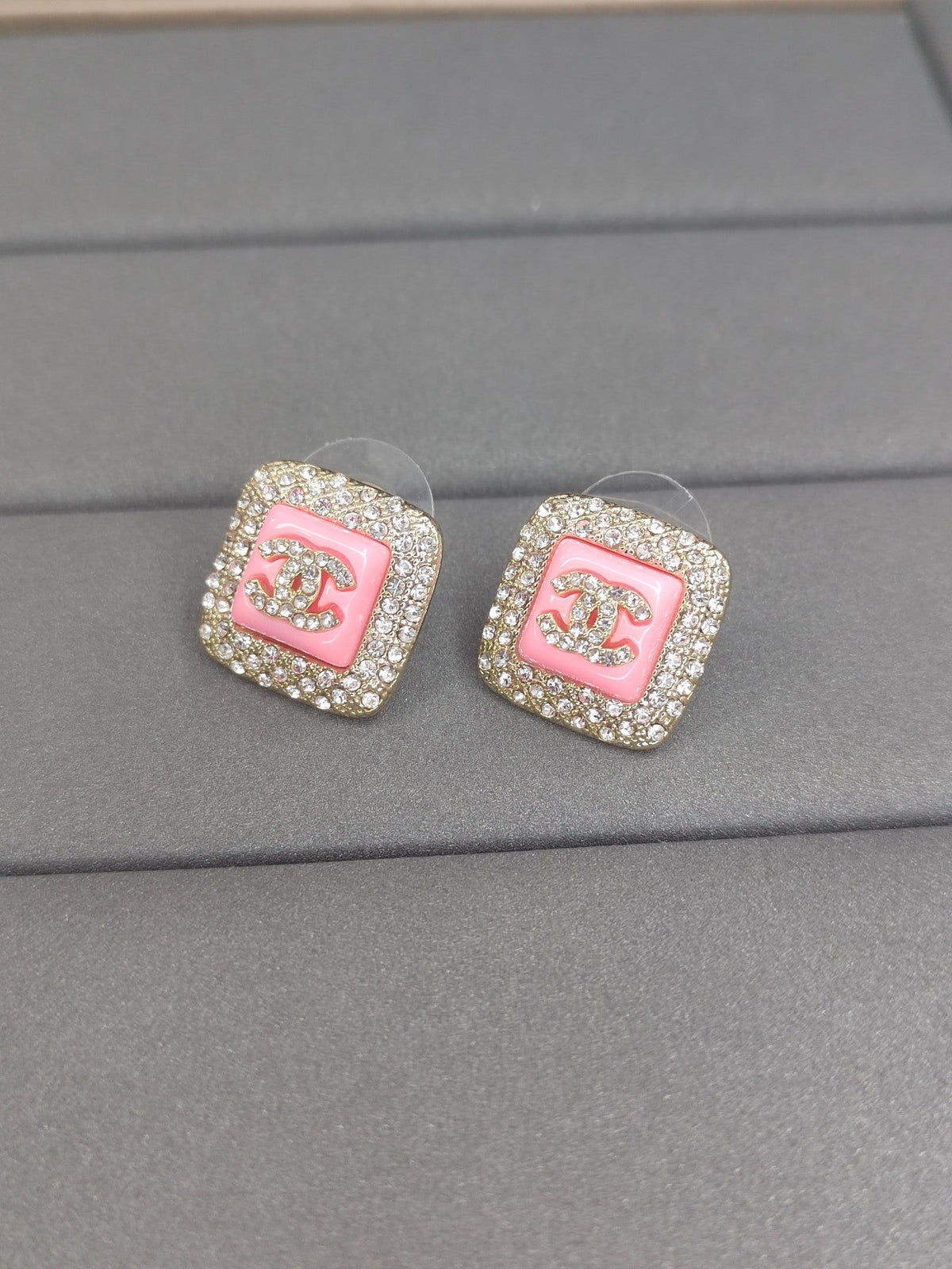 Pair of Chanel earrings with pink center and rhinestones on a gray surface