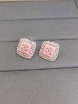 Pair of Chanel earrings with pink center and rhinestones on a gray surface