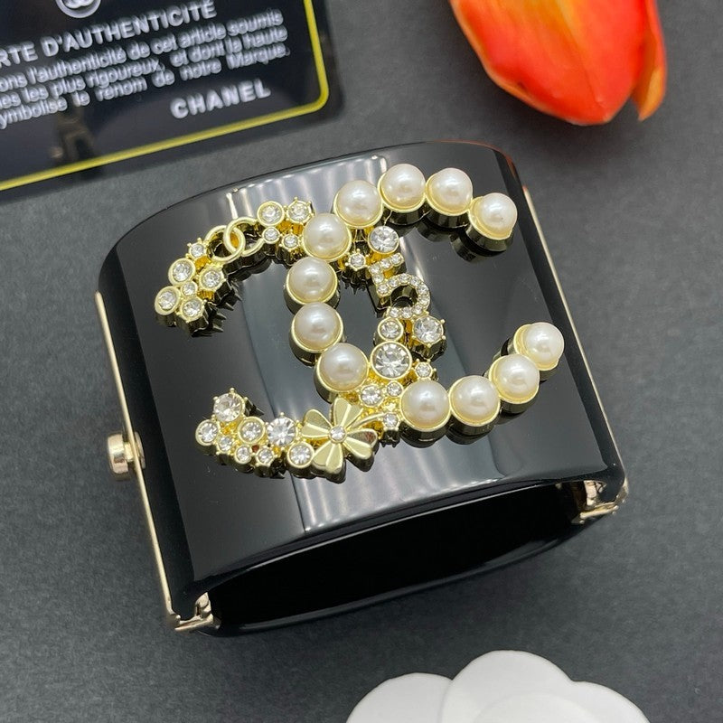 Black case with pearl and gold design on a gray surface, featuring Chanel branding.