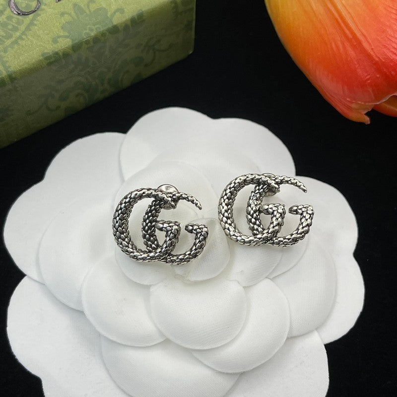 Silver 'GG' earrings on a white flower with a green box and orange tulip in the background