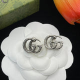 Silver 'GG' earrings on a white flower with a green box and orange tulip in the background