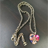Necklace with a heart-shaped pendant featuring a brand logo on a dark surface