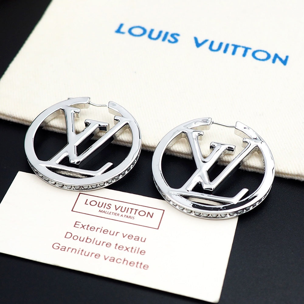 Silver earrings with Louis Vuitton logo on a black surface with a branded box in the background.