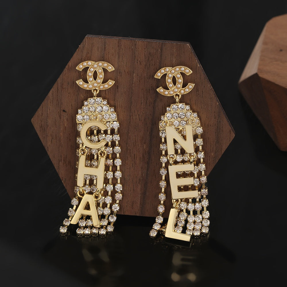 Gold Chanel earrings with diamond accents on a wooden stand against a dark background