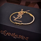 A gold-tone chain bracelet with a YSL logo charm and a row of clear stones, displayed on a black textured Yves Saint Laurent box.