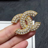 Gold and crystal brooch with Chanel logo held in a hand against a dark background